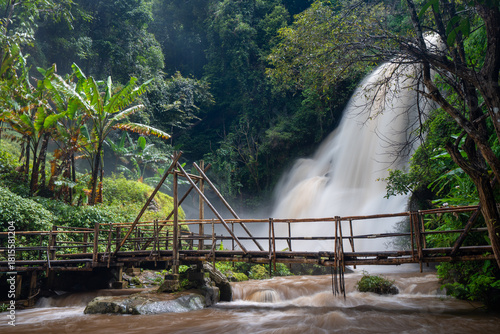 Fototapeta Pha Dok Siew Waterfall cascading through tropical rainforest with wooden footbri