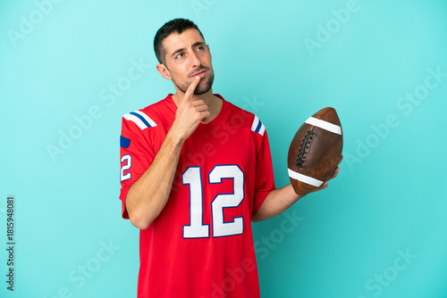 Young caucasian man playing rugby isolated on blue background having doubts while looking up