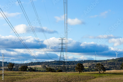 Powerlines and wires of the energy grid with wind turbines on ridgeline in farm land