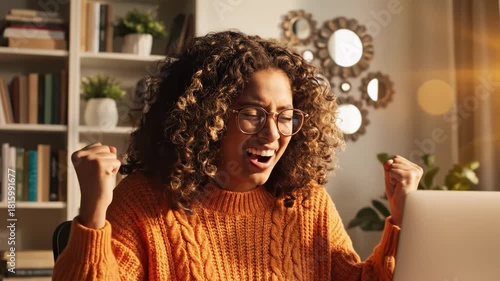 Excited woman celebrating success with arms raised in front of a laptop