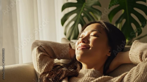 Relaxing woman enjoying sunlight indoors with a plant in the background