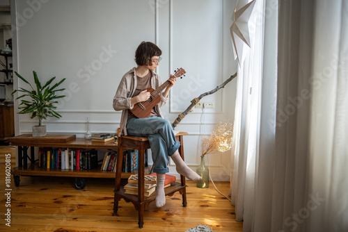 Absorbed woman musician practice ukulele string instrument by window, refining sequences. Creative dedicated practice, solo acoustic rehearsal, home musical discipline, female artist chord repetition