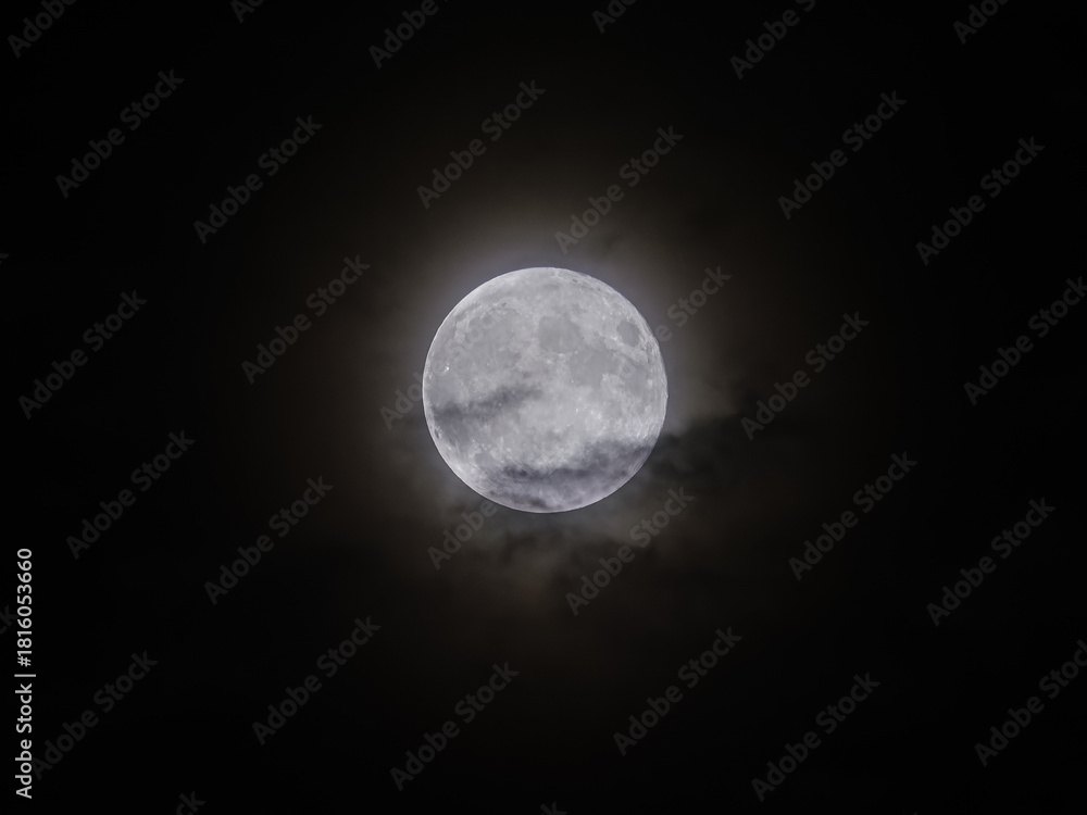 Fototapeta premium Glowing full Moon shines brightly in the dark Night Sky with a soft atmospheric Halo around it, captured from Earth.