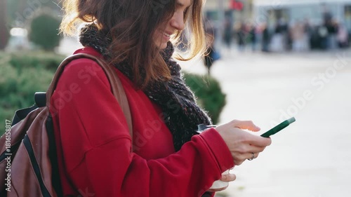 A pretty young woman uses her mobile phone while walking through the streets of a European city on a warm autumn day.