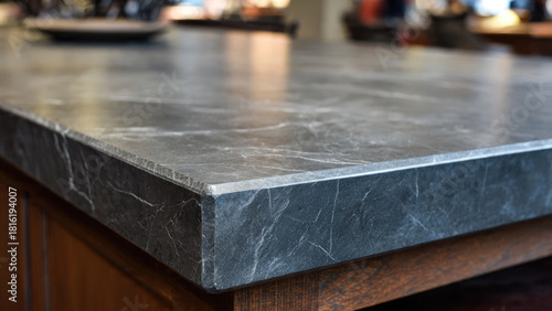 Close-up of a dark grey natural stone countertop with white veining, showcasing its elegant surface and textured edge above a wooden cabinet.