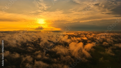A high-altitude aerial photograph capturing a sunrise above a vast forest with golden morning mist drifting through the treetops