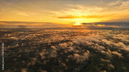 A high-altitude aerial photograph capturing a sunrise above a vast forest with golden morning mist drifting through the treetops