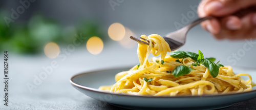 Obraz  z motywem Close-up of fork twirling creamy pasta with fresh basil leaves on a plate with blurred background