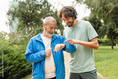 Senior father and son jogging doing sport together, checking cardio levels using smartwatch app after running in the morning