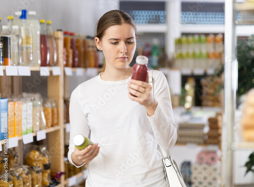 Girl customer in supermarket examines smoothie, chooses food-stuff in health lifestyle store