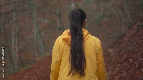 Slow motion camera follows active young brunette woman hiker in yellow jacket walking alone in the forest. Girl walking and enjoying outdoors nature in late autumn season