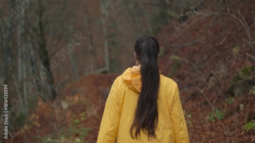 Slow motion camera follows active young brunette woman hiker in yellow jacket walking alone in the forest. Girl walking and enjoying outdoors nature in late autumn season