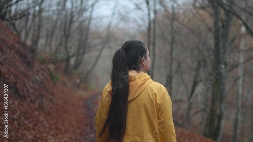 Slow motion camera follows active young brunette woman hiker in yellow jacket walking alone in the forest. Girl walking and enjoying outdoors nature in late autumn season