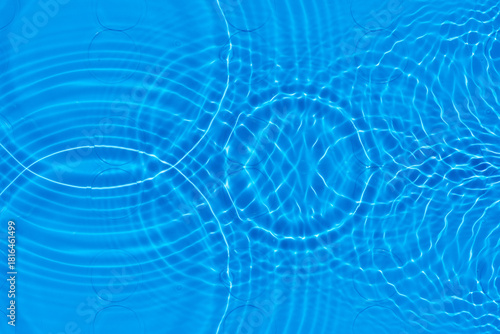 Blue water with ripples on the surface. Defocus blurred transparent blue colored clear calm water surface texture with splashes and bubbles. Water waves with shining pattern texture background.
