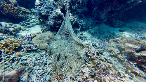 A discarded fishing net lies draped across a damaged coral reef. The abandoned mesh traps debris and highlights the harsh impact of marine pollution underwater.