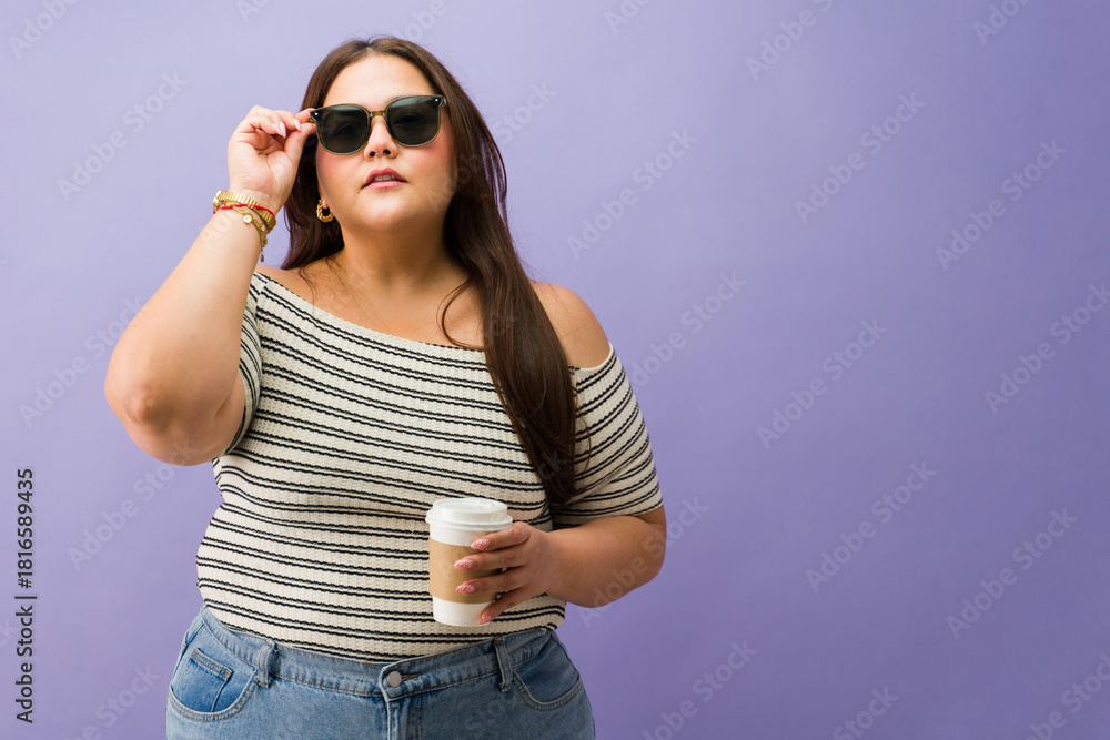 Fototapeta premium Curvy woman lifting sunglasses on purple background