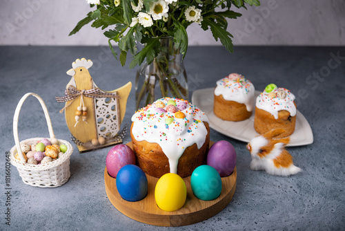 Easter kulich with candied fruits in white glaze with colorful sprinkles and painted eggs. Traditional Easter pastry. Easter holiday. Close-up, selective focus.