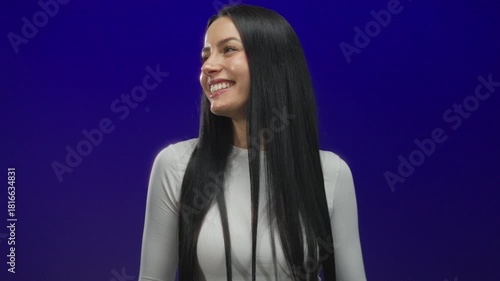 Wallpaper Mural Woman smiling in front of a vibrant blue wall wearing a white shirt, showcasing long black hair and a joyful expression, capturing a youthful and positive mood. Torontodigital.ca