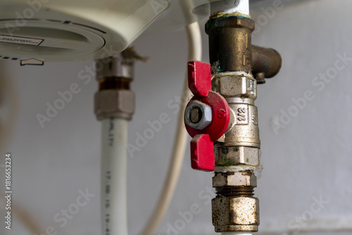 Red valve on  electric water heating boiler close up shot.