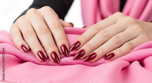 Woman's hands with dark red stiletto nails on pink fabric