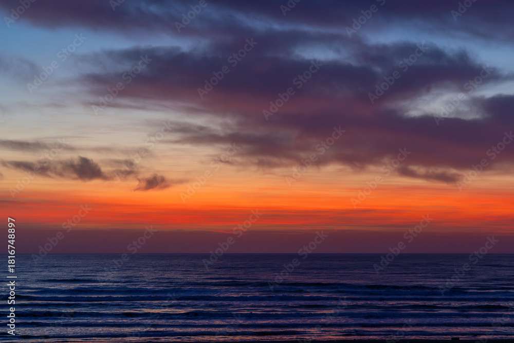 Naklejka premium A scenic view of a dramatic sunset or sunrise over the ocean, with vivid orange, red, and purple hues reflecting on gentle waves