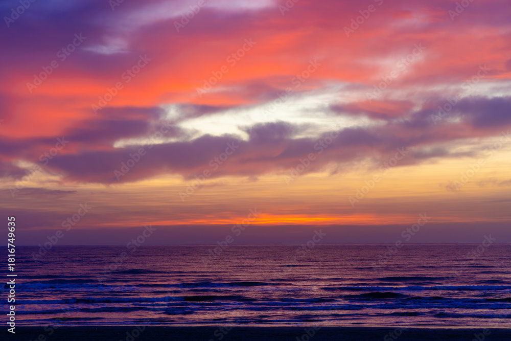 Obraz premium Landscape with a beautiful and vibrant sunset over the ocean, with the sky painted in various hues of orange, pink, purple, and yellow