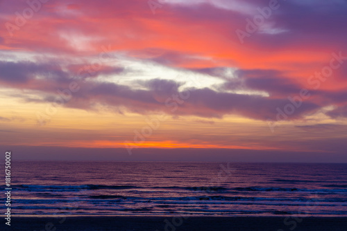 A beautiful and dramatic sunset over the ocean. The sky is filled with vibrant colors, ranging from deep purple and pink near the horizon to bright orange and red higher up