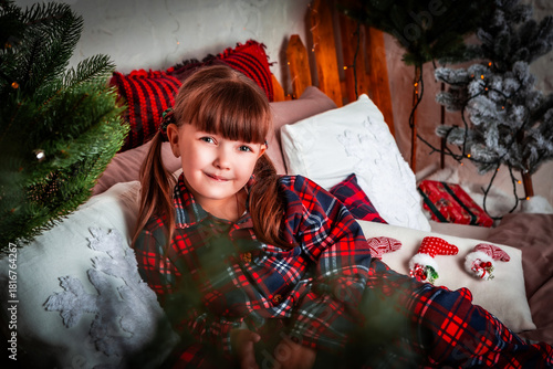 Happy little girl child in pajamas lies in bed in bedroom. Christmas. New Year. St. Nicholas Day. Time of holidays and miracles.	