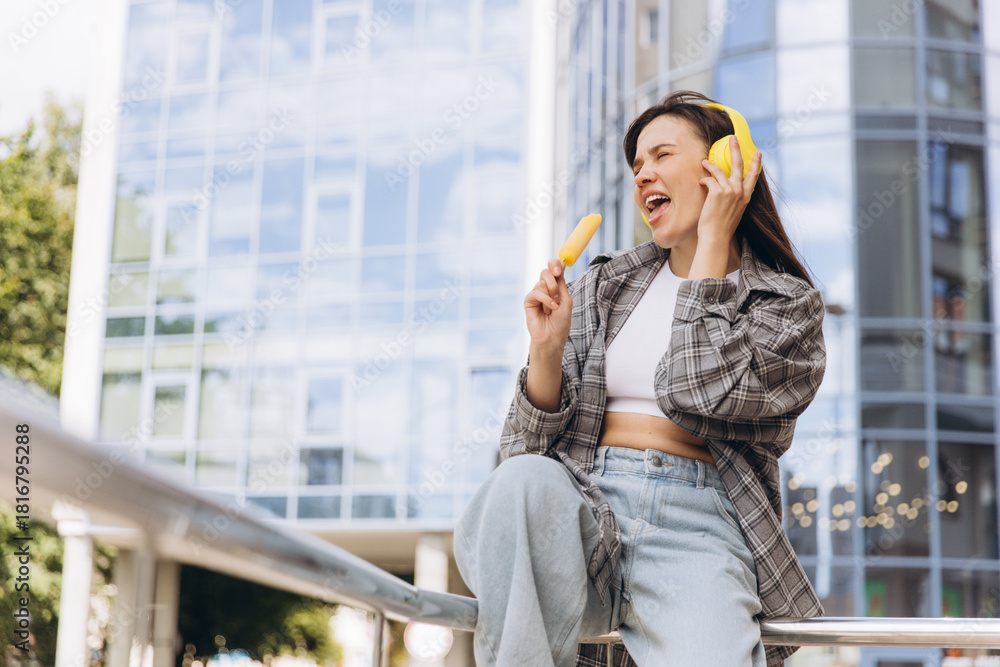 Fototapeta premium Woman singing with headphones and eating ice pop