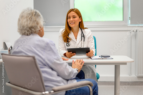 Фотография Smiling female doctor holding patient's records and listening to elderly woman d