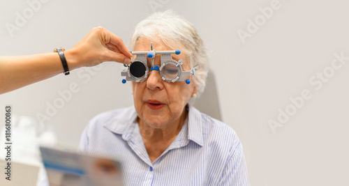 Female ophthalmologist's hand adjusting phoropter while senior woman reads eye chart during vision test at clinic