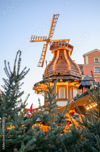 Vertical winter scene featuring a bright Christmas windmill surrounded by holiday decorations. Ideal for festive campaigns, tourism materials, market visuals, and seasonal advertising.
