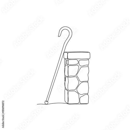 Rustic shepherd s crook leaning against a stacked stone pillar