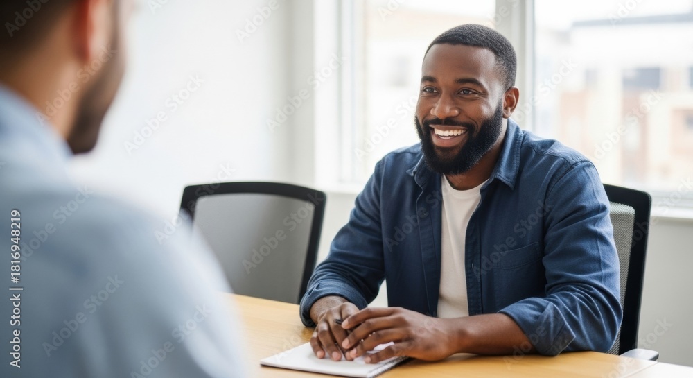 Naklejka premium A friendly and confident young professional man with a beard smiling happily while listening during a business meeting or job interview in a modern, sunlit office