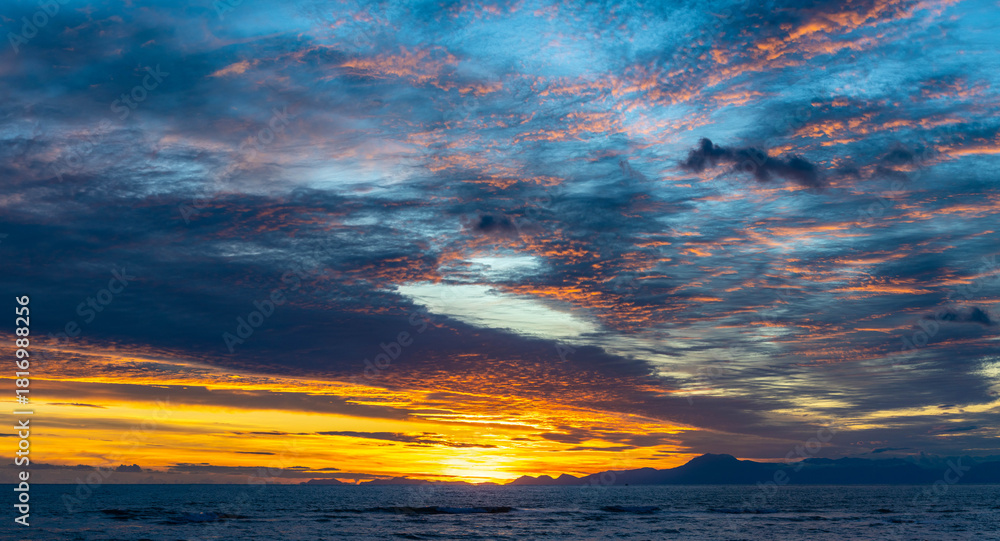 Fototapeta premium A picturesque sunset over the Mediterranean Sea in Side, with golden-lit clouds against a blue sky and dark blue waters. A stunning evening scene in Antalya, Turkey.