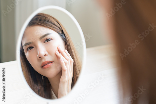 Anti aging, worry puberty asian young woman, stressed girl looking in mirror, allergy presenting an allergic reaction from cosmetic on face. Beauty, health care from acne problem, dry skin, treatment.