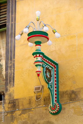 Colorful Ornate Street Lamp With Green Red Details Mounted on Yellow Stucco Wall Historic Facade