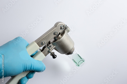 Photography scientist's hand using a manual vial crimper tool to seal an aluminum cap onto a glass autosampler vial containing a green liquid sample