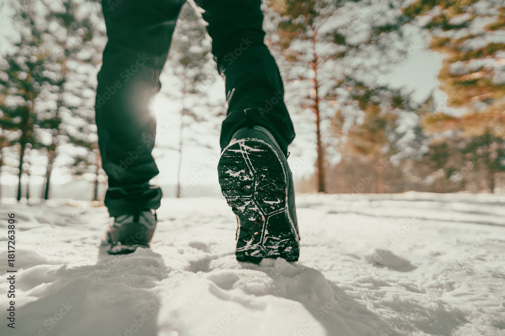 Fototapeta premium A winter walk through a snowy forest. A close-up of a person's feet in winter boots walking through the snow on a sunny, frosty day. The image conveys a sense of fresh air, outdoor activity