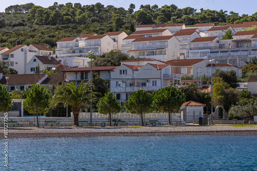 Fototapeta Naklejka Na Ścianę i Meble -  Coastal Village With White Houses, Red Roofs, Palm Trees, And Boats Docked By The Shore, Necujam, Croatia