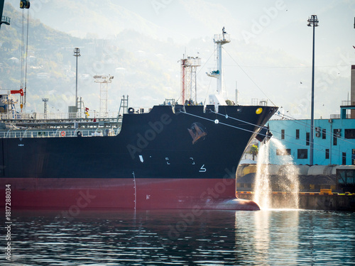 Cargo ship moored at port with ballast water discharge, maritime logistics and shipping industry.