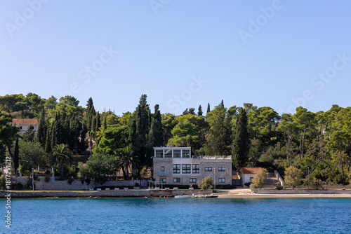 Fototapeta Naklejka Na Ścianę i Meble -  Seaside Villa With Lush Trees On a Calm Blue Coastline Under Clear Sky, Necujam, Croatia