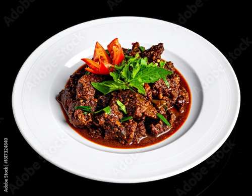 Beef rendang on a white plate. Isolated on a black background.