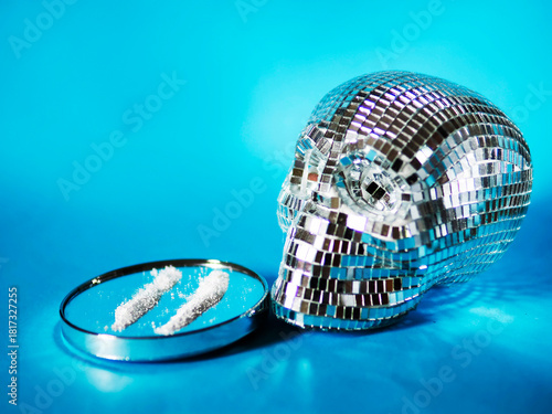 A skull is on a blue background with a pair of white powdery substances on a glass plate. Party drugs or illegal powder. Criminal activity and black market.