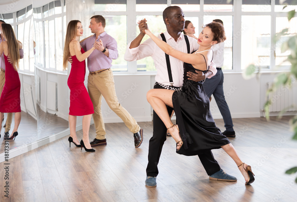 Naklejka premium Woman paired with African American man practices movements of Latin tango dance and trains to perform movements during lesson in choreography studio.