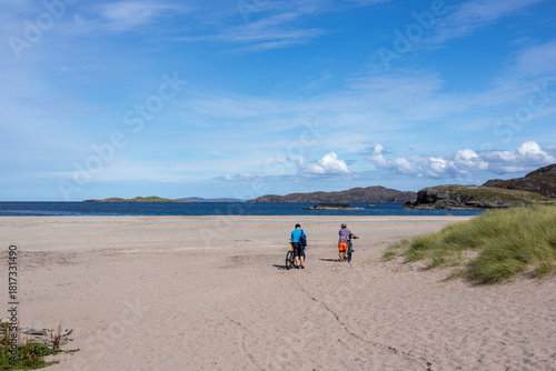 Foto Two distant cyclists walking their bikes across an empty Clashnessie beach in northern Scotland on a late summer afternoon
