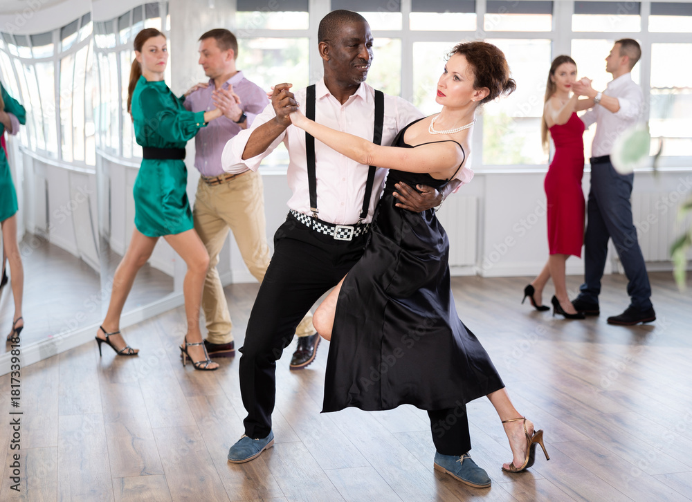 Fototapeta premium Pair of woman and African American man enjoying of sensual tango dance in choreo class. Exciting hobby, active lifestyle, passion for dancing and choreography
