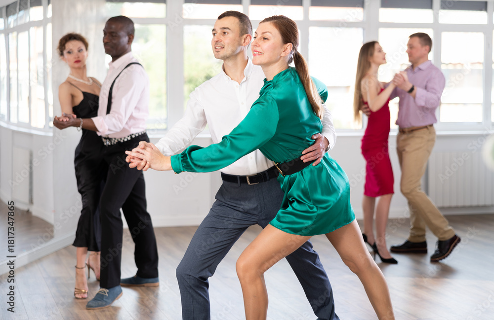 Fototapeta premium Dynamic young male and female attendees of dancing courses doing waltz in group