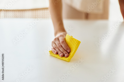Foto Cleaning hand using a yellow cloth to wipe a white table surface in home interior, closeup of person performing household chores and tidy maintenance for sanitation and care