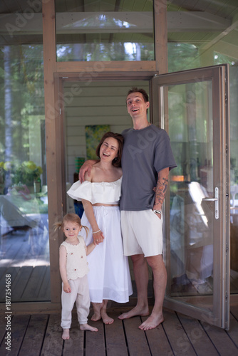 Fotografía A family stands on a wooden porch of their summer home, surrounded by greenery
